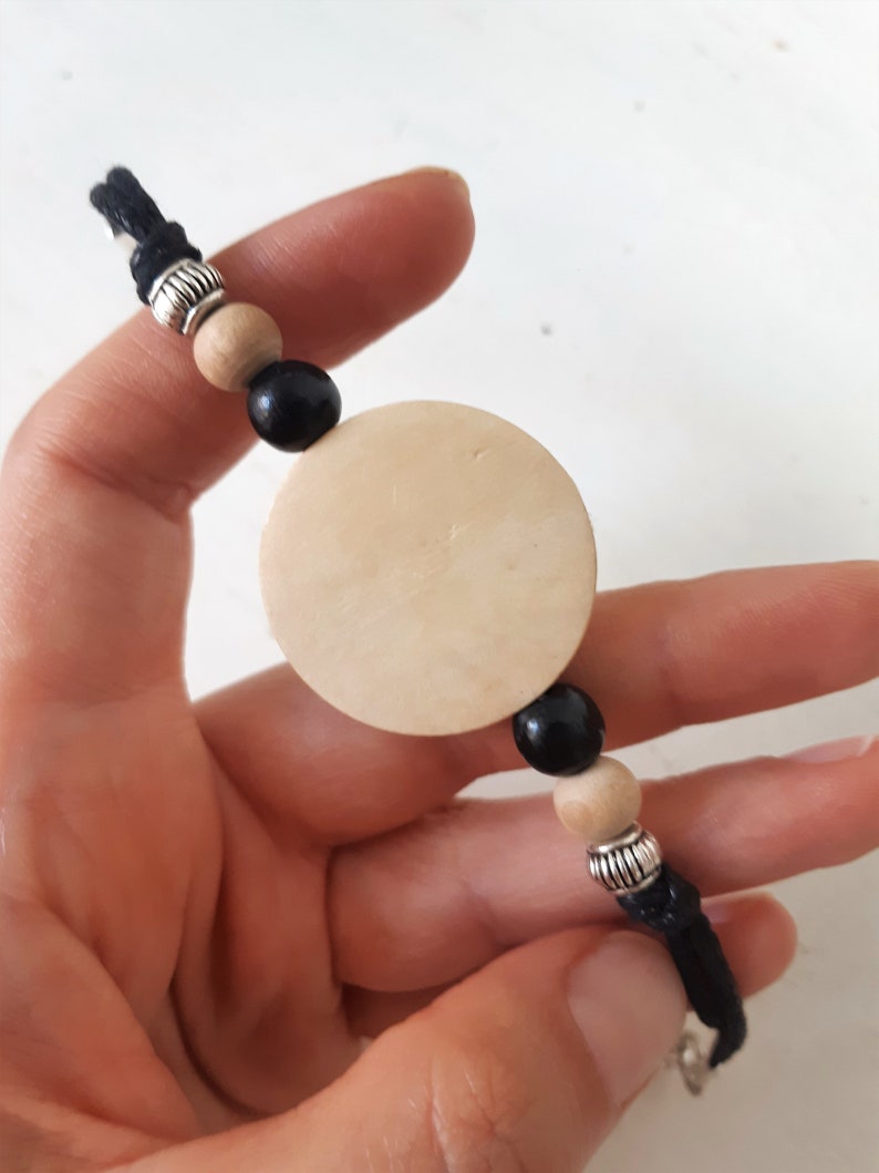 Puede incluir: Un brazalete de cord&oacute;n negro con cuentas de madera y plata y un gran dije redondo de madera.
