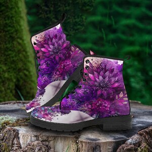 Może przedstawiać: Para czarno-białych botków z kwiatowym wzorem w kolorze fioletowym, ze sznurowaniem i czarną podeszwą. Buty stoją na pniu drzewa.