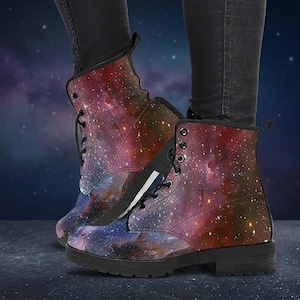 May include: A pair of lace-up ankle boots with a vibrant galaxy print in shades of red, purple, and blue. The boots have a black sole and are worn with black pants. The boots appear to be made of a durable material.