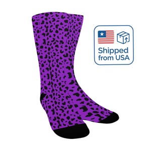 May include: A pair of knee-high socks with a purple background and black leopard print pattern. The socks have black heels and toes. The image includes a graphic that says "Shipped from USA".