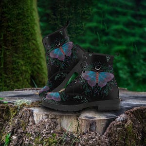 Pode incluir: Botas de combate pretas com um design de borboleta em roxo e azul-petr&oacute;leo. As botas t&ecirc;m fecho de atacadores e biqueira redonda. O design da borboleta &eacute; colocado sobre um fundo de folhagem verde e uma lua crescente. Altura: aprox. 25 cm.