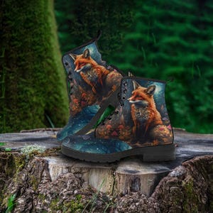 May include: A pair of combat boots featuring a detailed illustration of a fox in a forest setting. The boots have a black sole and laces, with a dark blue and brown color scheme. The fox is depicted with orange and white fur.