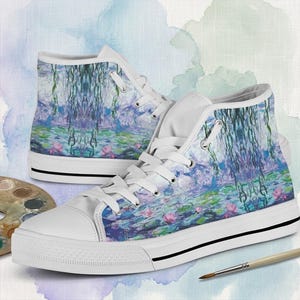 May include: White high-top sneakers featuring a colorful impressionist painting design. The artwork depicts a water lily pond with pink flowers, green lily pads, and weeping willow trees. The shoes have white laces, a white rubber sole, and a black stripe.