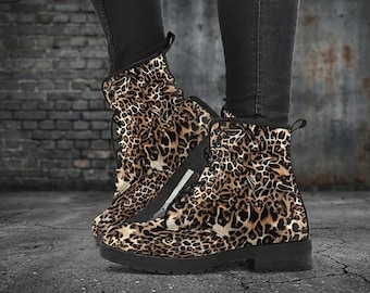 May include: A pair of ankle boots with a leopard print pattern. The boots have a black sole and laces. The background is a dark brick wall and a concrete floor.