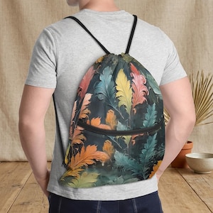 May include: A drawstring backpack with a colorful feather pattern. The bag features a black zipper and black drawstrings. The feathers are in shades of orange, yellow, blue, and green against a dark background. The bag is worn over the shoulders.