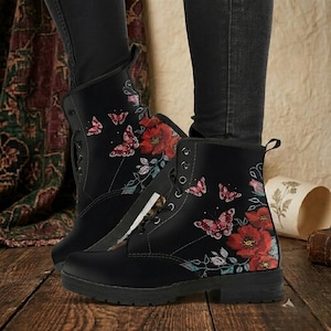 Puede incluir: Botas de combate negras con diseño floral y de mariposas. Las botas presentan amapolas rojas y mariposas rosas, con cordones en la parte delantera y una suela resistente. Las botas están hechas de un material duradero.