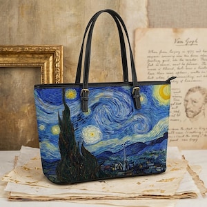 May include: A tote bag featuring a print of Vincent van Gogh's "Starry Night" painting. The bag has black handles and trim, with a zipper closure. The artwork depicts a swirling night sky with stars, a crescent moon, and a village.