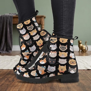 May include: Black combat boots with a repeating pattern of cartoon cat faces in various colors and expressions. The boots have black laces and soles. The cat faces include cats with glasses, bow ties, and different colored fur.