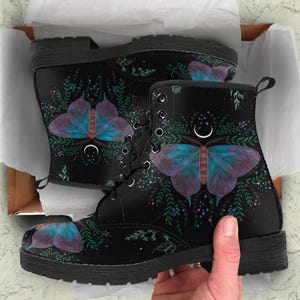 Pode incluir: Botas de combate pretas com um design de borboleta em tons de azul, roxo e vermelho. As botas t&ecirc;m fecho de atacadores e sola resistente. A borboleta &eacute; rodeada por detalhes florais e celestiais.
