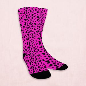 May include: A pair of knee-high socks with a vibrant pink background and a black leopard print pattern. The socks have black heels and toes, offering a bold contrast. These socks are a fun and fashionable accessory.