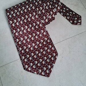 May include: A burgundy and white patterned silk tie with a wavy design.