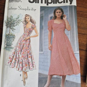 Könnte beinhalten: Eine Simplicity-Schnittmusterhülle mit einem Vintage-Kleiderdesign. Das Cover zeigt eine Illustration eines Blumenkleides und ein Foto eines roten Kleides mit weißem Muster, beide mit Puffärmeln und einem herzförmigen Ausschnitt versehen.