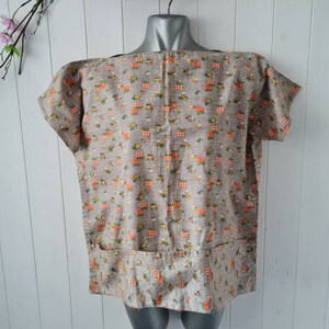 May include: A brown and white short-sleeved blouse with a floral print. The blouse has a pocket on the front and a boat neck.