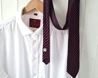May include: A white dress shirt with a red and blue striped tie hanging on a wooden hanger. The tie has a small label with the text "48" on it. The shirt has a label with the text "Scott & Taylor" on it.