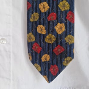 May include: A navy blue tie with a repeating pattern of red and yellow floral designs. The tie is set against a white shirt, showcasing the vibrant colors and textured fabric. The tie's design is a classic accessory.
