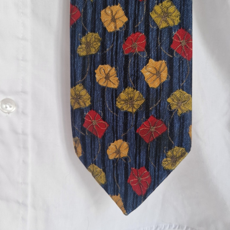 May include: A navy blue tie with a repeating pattern of red and yellow floral designs. The tie is set against a white shirt, showcasing the vibrant colors and textured fabric. The tie's design is a classic accessory.
