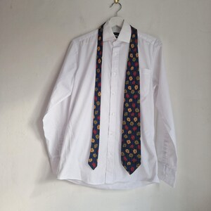 May include: A crisp white long-sleeved button-down shirt with a pointed collar, displayed with a dark blue necktie featuring a repeating pattern of small red and yellow floral shapes hanging down the front of the garment.