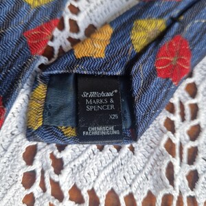 May include: Close-up of a blue tie with a floral pattern in red and yellow. The tie has a textured appearance and features a label with the text "St Michael MARKS & SPENCER". The label also includes the text "CHEMISCHE FACHREINIGUNG".