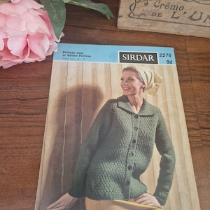 May include: A knitting pattern for a green cardigan with a button closure. The pattern is from Sirdar and is for sizes 34-40 inches. The pattern is called 2276 and costs 9d.