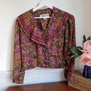 以下が含まれることがあります： バーガンディカラーの襟と長袖が付いた、ヴィンテージの花柄ブラウス。ブラウスはボタン留めになっており、Jessica Howard製です。