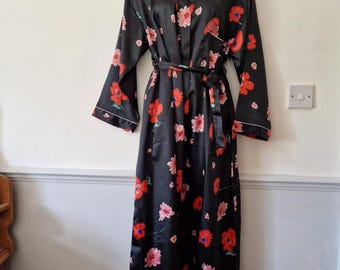 May include: A black satin robe with a floral print featuring red and pink flowers. The robe has a long, flowing silhouette and a tie belt.
