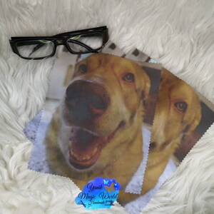 May include: Black framed eyeglasses rest on a white fluffy surface next to two microfiber cleaning cloths. The cloths feature a close-up image of a smiling yellow Labrador Retriever dog. The logo "Yanik Magic World Handmade" is visible.