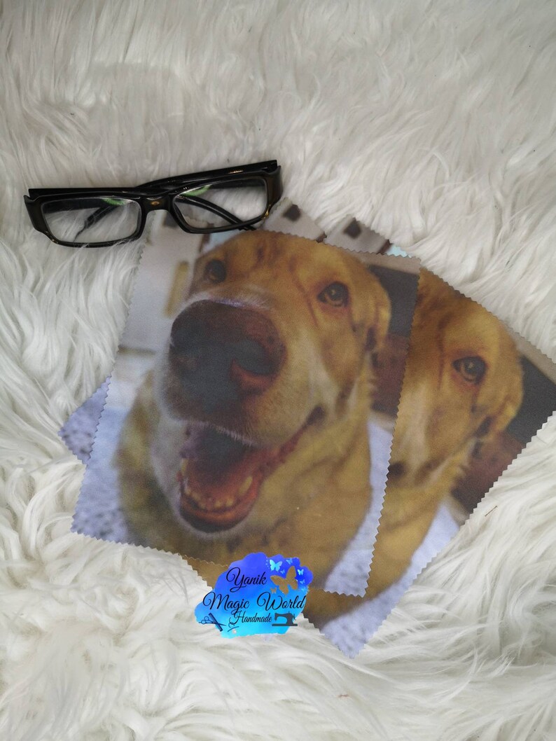 May include: Black framed eyeglasses rest on a white fluffy surface next to two microfiber cleaning cloths. The cloths feature a close-up image of a smiling yellow Labrador Retriever dog. The logo "Yanik Magic World Handmade" is visible.