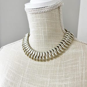May include: A silver-toned metal necklace with a chain link design. The necklace is on a white mannequin.