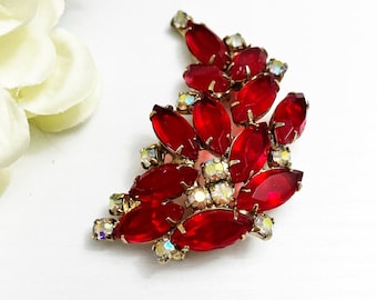 Pode incluir: Broche vintage com um grupo de strass vermelhos com corte marquesa e pedras iridescentes menores, cravejados em metal dourado. O broche tem um design em forma de folha, com as pedras vermelhas dispostas para se assemelharem a pétalas.