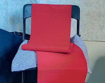 Puede incluir: Una tela larga de color rojo brillante está doblada y drapeada sobre una silla plegable de metal negro. La tela es lisa y parece ser de seda o satén.