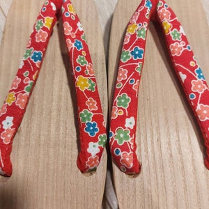 May include: A pair of red wooden sandals with floral patterned straps. The sandals have a traditional Japanese design.