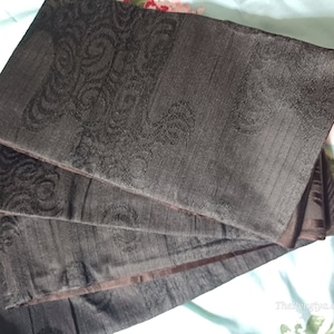 Può includere: Un set di quattro tovagliette da tavola in tessuto nero con un delicato motivo in rilievo. Le tovagliette sono piegate a metà e hanno una texture morbida e vellutata.