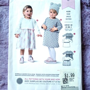 Op de afbeelding: Een Burda Kids naaipatroonpakket met illustraties van twee kinderen in jurken. Het pakket bevat de tekst "KLEID ROBE DRESS VESTIDO" en maat informatie. Het prijskaartje toont $1,99.