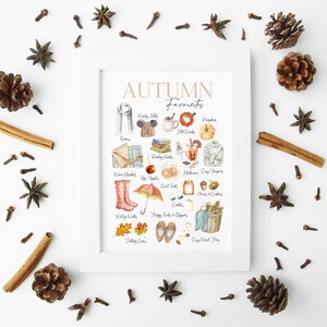 K&ouml;nnte beinhalten: Ein wei&szlig;er gerahmter Druck mit dem Titel "AUTUMN Favourites" und einer Aquarellillustration verschiedener Herbstmotive, darunter K&uuml;rbisse, Bl&auml;tter, Stiefel und eine gem&uuml;tliche Decke.