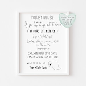 May include: A framed white print with black text that reads "TOILET RULES" followed by humorous instructions. A heart-shaped graphic states "AVAILABLE IN MULTIPLE SIZES & FINISHES". A roll of toilet paper is illustrated.