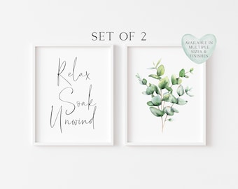 May include: A set of two framed wall art prints. The left print features the black text Relax Soak Unwind in a script font. The right print displays a watercolour illustration of green eucalyptus leaves. A heart-shaped badge states SET OF 2 and AVAILABLE IN MULTIPLE SIZES & FINISHES.