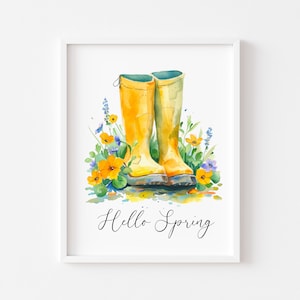 May include: Watercolour print featuring yellow wellington boots amidst orange and purple flowers and foliage. The cursive text "Hello Spring" is below the boots. The artwork is presented in a white frame.