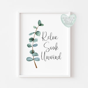 Puede incluir: Una impresi&oacute;n enmarcada con las palabras "Relax Soak Unwind" en escritura cursiva, acompa&ntilde;ada de una rama de eucalipto en acuarela. Una etiqueta en forma de coraz&oacute;n en la esquina superior derecha dice "Available in Multiple Sizes & Finishes".