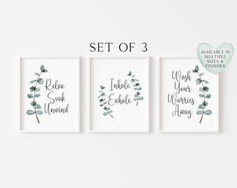 May include: A set of three white-framed wall art prints featuring watercolour eucalyptus branches and black script text. The prints read Relax Soak Unwind, Inhale Exhale, and Wash Your Worries Away. A heart-shaped badge states Available in Multiple Sizes & Finishes.