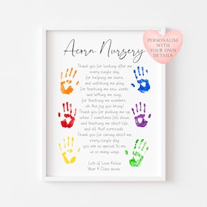 May include: A framed print with the text "Acorn Nursery" and a poem with colorful handprints. The print includes the text "Personalise with your own details" on a heart-shaped graphic. The bottom of the print reads "Lots of Love Kelsie Year 4 Class seven."