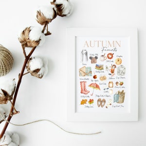 K&ouml;nnte beinhalten: Ein wei&szlig;er gerahmter Druck mit dem Text "AUTUMN Favourites" in braunen Buchstaben. Der Druck zeigt eine Sammlung von Aquarell-Illustrationen von Herbstgegenst&auml;nden, darunter ein K&uuml;rbis, Bl&auml;tter, Stiefel und eine Tasse hei&szlig;e Schokolade.