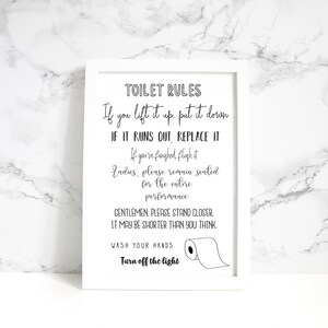 May include: A framed white sign with black text that reads "TOILET RULES." The sign includes humorous instructions such as "If you lift it up, put it down" and "Gentlemen, please stand closer." A roll of toilet paper is illustrated.