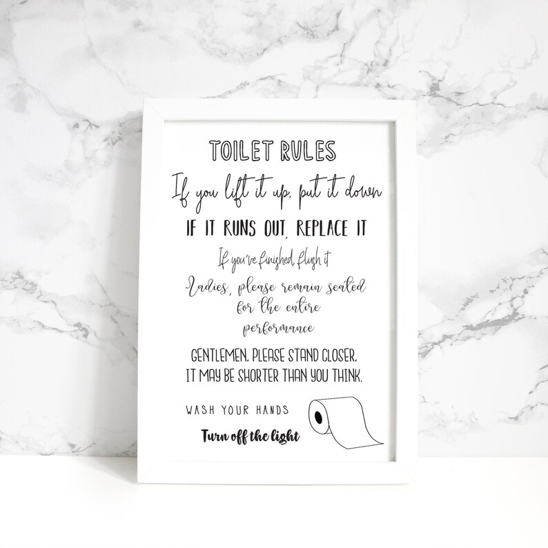 May include: A framed white sign with black text that reads "TOILET RULES." The sign includes humorous instructions such as "If you lift it up, put it down" and "Gentlemen, please stand closer." A roll of toilet paper is illustrated.