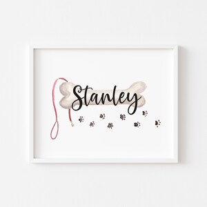 May include: A white bone-shaped print with the name "Stanley" written in black cursive. The bone has a red leash attached to it and there are several brown paw prints scattered below.