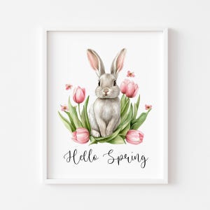 May include: A framed watercolour print showing a grey rabbit amidst pink tulips and green leaves. The words "Hello Spring" are written in elegant script below the rabbit. The artwork is set against a white background.