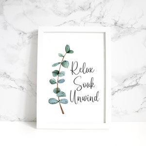 Puede incluir: Una impresi&oacute;n enmarcada con borde blanco presenta una rama de eucalipto en acuarela y las palabras "Relax, Soak, Unwind" en escritura elegante. La obra de arte tiene una est&eacute;tica relajante, tipo spa, ideal para la decoraci&oacute;n de ba&ntilde;o o dormitorio.