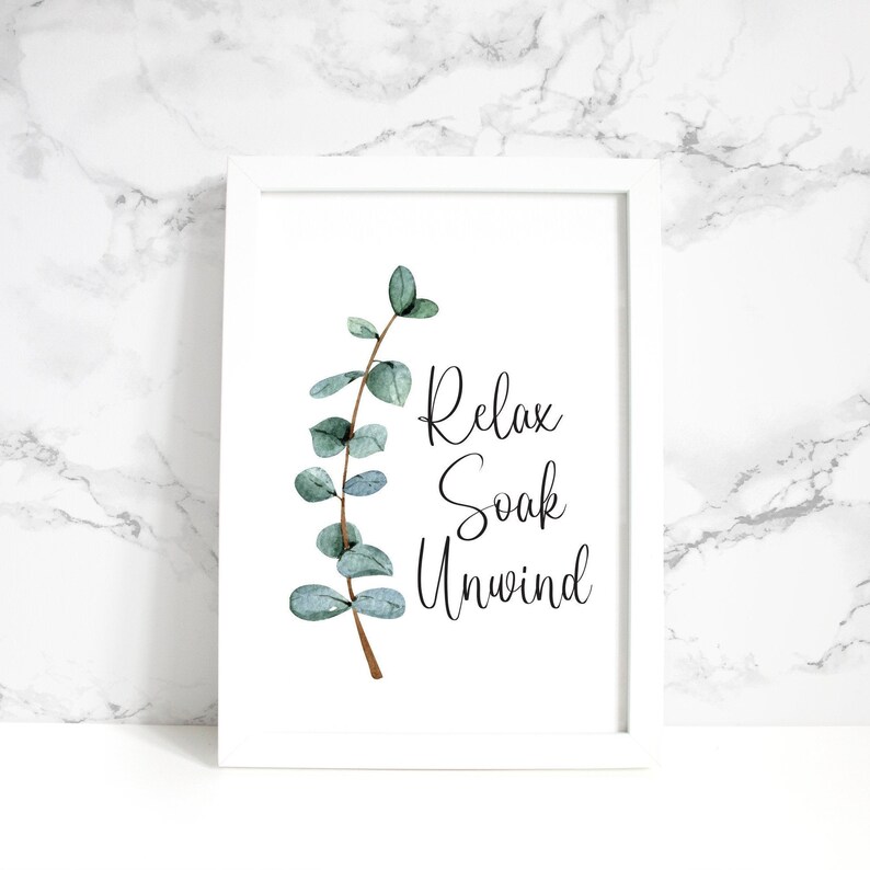 Puede incluir: Una impresi&oacute;n enmarcada con borde blanco presenta una rama de eucalipto en acuarela y las palabras "Relax, Soak, Unwind" en escritura elegante. La obra de arte tiene una est&eacute;tica relajante, tipo spa, ideal para la decoraci&oacute;n de ba&ntilde;o o dormitorio.