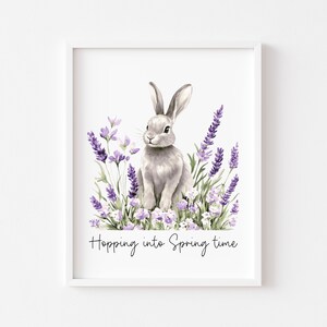 May include: A framed watercolour print showing a grey rabbit surrounded by lavender flowers. The artwork has a soft, pastel colour palette with the text "Hopping into Spring time" at the bottom. The print is in a white frame.