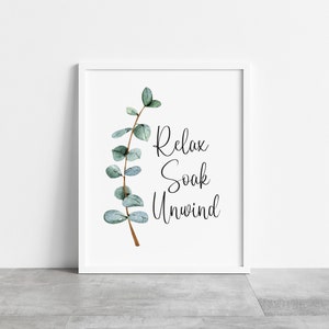 Puede incluir: Una impresi&oacute;n enmarcada en blanco con las palabras "Relax, Soak, Unwind" en escritura negra. Una ilustraci&oacute;n de acuarela de una rama de eucalipto con hojas verdes y verde azulado est&aacute; a la izquierda. El marco es blanco.
