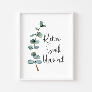 Puede incluir: Una impresi&oacute;n enmarcada con una rama de eucalipto en acuarela, con hojas verdes y un tallo marr&oacute;n. Las palabras "Relax, Soak, Unwind" est&aacute;n escritas en escritura negra. La impresi&oacute;n est&aacute; enmarcada en un marco blanco.